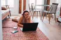 Молода жінка лежить на підлозі вдома і використовує ноутбук — стокове фото