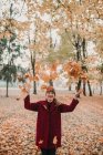 Femme élégante en manteau rouge vomissant des feuilles tombées colorées dans le parc et riant — Photo de stock