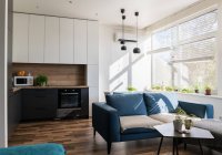 Sofá confortável em pé perto de móveis de cozinha em quarto elegante do apartamento moderno no dia ensolarado — Fotografia de Stock