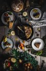 Dall'alto vista di tortilla saporita su pentola vicino a piatti con fette, pomodori, frutta, noci e foglie su asse di legno — Foto stock