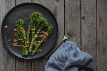 Steamed broccoli with romesco sauce on black plate with fork on wooden table — Stock Photo