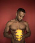 Retrato de un hombre afroamericano musculoso parado sin camisa y sosteniendo melón - foto de stock