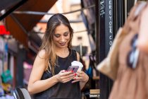 Mujer con bebida y smartphone cerca de la cafetería al aire libre - foto de stock