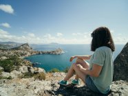 Pensive woman sitting on rocky coastline and looking at view — Stock Photo