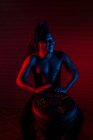 Joven rastafari africano hombre disfruta ensayando y juega tam tam, iluminación de color rojo y azul - foto de stock