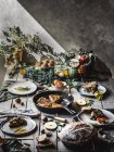 Dall'alto vista di tortilla saporita su pentola vicino a piatti con fette, pomodori, frutta, noci e foglie su asse di legno — Foto stock