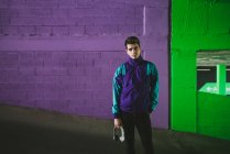 Молодий красивий чоловік у спортивній куртці з гарнітурою, що стоїть на тлі барвистої стіни і дивиться на камеру — стокове фото