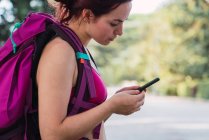 Sportswoman with pink backpack browsing smartphone in park — Stock Photo