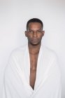 Porträt eines selbstbewussten schwarzen Mannes in weißes Laken auf weißem Hintergrund gehüllt — Stockfoto