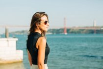 Young brunette woman standing on seafront and looking at view — Stock Photo