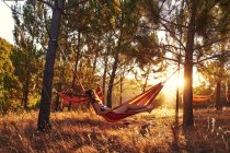 Donna sdraiata in amaca nei boschi soleggiati — Foto stock