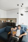 Молодой человек и женщина обнимают друг друга и наслаждаются хорошей пленкой на ноутбуке, сидя на удобном диване в уютной гостиной — стоковое фото