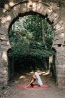 Woman standing in Downward-Facing Dog pose while doing yoga under old crumbling arch — Stock Photo