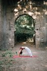 Mujer doblando hacia atrás mientras que hace yoga bajo viejo arco que se desmorona - foto de stock