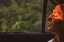 Vue latérale d'une jolie jeune femme gardant les yeux fermés alors qu'elle était assise à l'intérieur d'un véhicule moderne pendant son voyage en Bulgarie et dans les Balkans — Photo de stock
