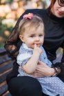 Portrait de bébé fille sucer pouce tandis que assis sur mère genoux à l'extérieur — Photo de stock