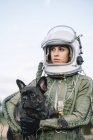 Smiling girl wearing old space helmet and spacesuit holding dog in nature — Stock Photo
