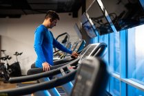 Joven en jersey deportivo azul haciendo ejercicio en la cinta de correr en el gimnasio - foto de stock