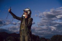 Усміхнений жіночий астронавт бере мобільний телефон у вечірній природі — стокове фото