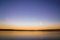 Paisagem de lago calmo com árvores no horizonte sob céu claro e sem nuvens ao pôr do sol — Fotografia de Stock