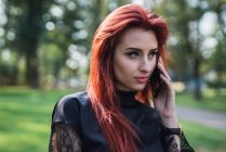 Young woman with ginger hair talking on smartphone in sunny park — Stock Photo