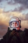 Улыбающаяся женщина-астронавт, использующая мобильный телефон против неба заката — стоковое фото