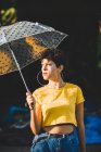 Jovem mulher pensativa com guarda-chuva transparente, enquanto em pé na rua no dia ensolarado — Fotografia de Stock