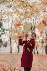 Elegante donna in cappotto rosso che vomita foglie colorate cadute nel parco e ride — Foto stock