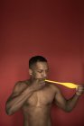Muscular shirtless black man blowing bright yellow balloon on red background — Stock Photo