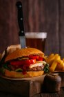 Delicious gourmet burger with knife on wooden board with beer and fries — Stock Photo
