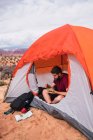 Homem de colheita com tigela de salada fresca sentado na tenda moderna na área de acampamento no deserto — Fotografia de Stock