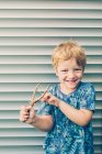 Biondo bambino in t-shirt giocare con fionda contro persiane — Foto stock