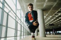 Porträt eines jungen Mannes in Sportbekleidung, der auf einem Geländer in einem Gebäude mit Säulen steht — Stockfoto