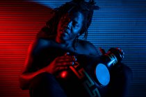 Jeune homme rastafari africain aime répéter et joue udu, éclairage coloré rouge et bleu — Photo de stock