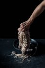 Человеческая рука, держащая осьминога над пластиной на черном мраморном фоне — стоковое фото