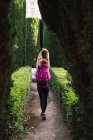 Rückansicht einer Sportlerin mit rosa Rucksack, die bei Tageslicht im Park zwischen sattgrünen Büschen spaziert — Stockfoto