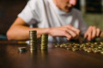 Anonymer junger Mann zählt glänzende Münzen und stapelt sie auf Holztisch — Stockfoto