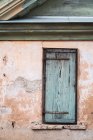 Narrow window with shabby timber shutter on crumbling wall of old house — Stock Photo