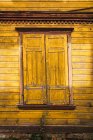 Janela com persianas fechadas localizadas na parede de madeira da casa rural amarela — Fotografia de Stock
