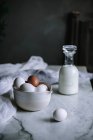 Schüssel mit Hühnereiern und Flasche frischer Milchprodukte steht auf Marmortischplatte in der Küche — Stockfoto