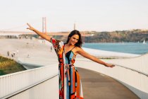 Elegante donna in abito in piedi sul ponte con le braccia tese e guardando la fotocamera — Foto stock