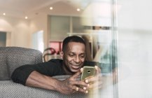 Afrikanisch-amerikanischer Mann benutzt Smartphone auf Sofa zu Hause — Stockfoto