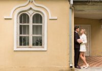 Side view of elegant bride and groom embracing near small old house in green garden — Stock Photo