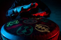 Giovane percussionista pratica tecnica con tam tam o tamburo, illuminazione colorata in rosso e blue.hands vista — Foto stock