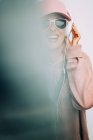 Woman in pink outfit and sunglasses listening to music on blurred background — Stock Photo