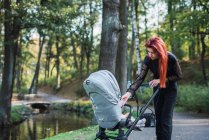Jovem mulher elegante andando com carrinho de bebê no parque — Fotografia de Stock