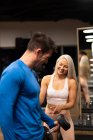 Frau hilft Mann beim Turnen mit Hantel im Fitnessstudio — Stockfoto