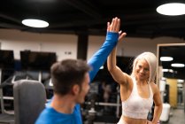 Gut gelaunte Männer und Frauen in Sportkleidung stehen im Fitnessstudio neben Geräten und machen High-Five-Gesten — Stockfoto