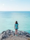 Woman in shorts standing on edge of cliff above endless blue sea water — Stock Photo
