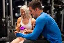 Athletic man and woman using smartphone in gym — Stock Photo
